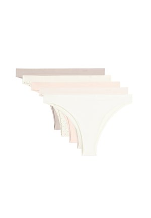 Femme portant des sous-vêtements beige sans coutures taille basse, montrant le torse du nombril aux cuisses sur un fond uni.