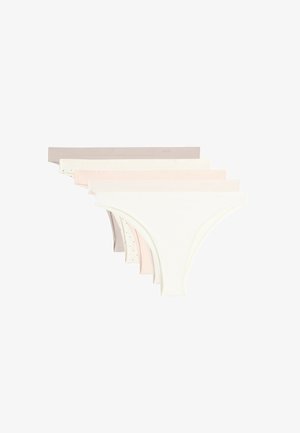 Femme portant des sous-vêtements beige sans coutures taille basse, montrant le torse du nombril aux cuisses sur un fond uni.