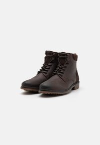 Botas de tobillo de cuero marrón con un acabado texturizado, cuello acolchado y acentos de gamuza en contraste. Suela de goma con relieve para mayor agarre.
