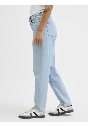 Person wearing light blue straight-leg jeans, white sneakers with black stripes, and a white shirt, standing against a plain background.