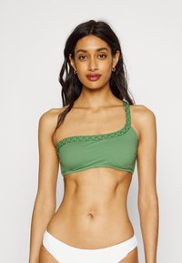 Top de biquíni verde com um ombro, feito de um tecido suave e elástico com um acabamento em trançado texturizado. Apresenta um design cropped e ajuste ajustável.