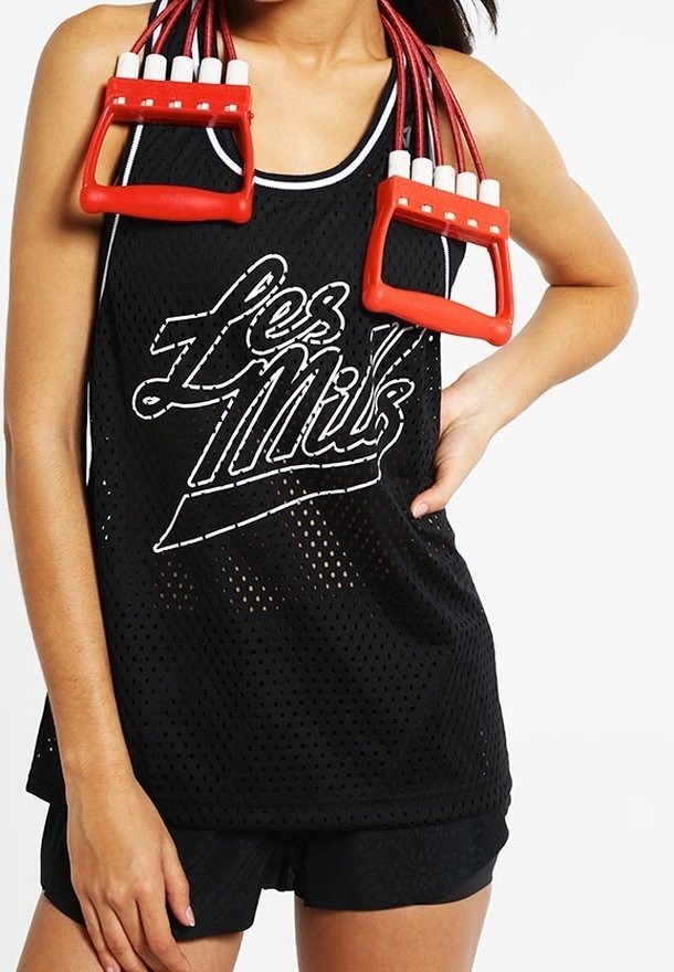 Schwarzes Mesh-Tanktop mit weißen "Les Mills"-Buchstaben, kombiniert mit schwarzen Shorts. Rotes Springseil mit weißen Griffen über den Schultern gelegt.