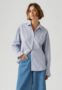 Camicia azzurro chiaro a righe con colletto classico e maniche lunghe, abbinata a pantaloni a gamba larga in denim blu a vita alta.