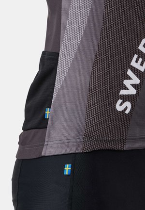 Nahaufnahme von grau-schwarzer Sportbekleidung mit atmungsaktivem Mesh-Gewebe, auf der kleine schwedische Flaggenetiketten an Ober- und Unterbekleidung zu sehen sind.
