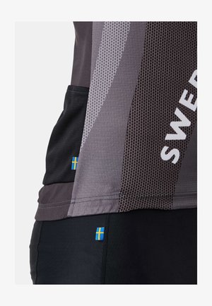 Nahaufnahme von grau-schwarzer Sportbekleidung mit atmungsaktivem Mesh-Gewebe, auf der kleine schwedische Flaggenetiketten an Ober- und Unterbekleidung zu sehen sind.