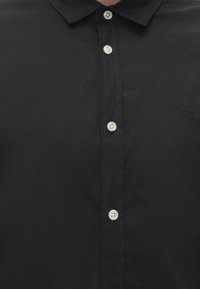 Black button-up shirt with a collar and five white buttons down the center front, showing subtle stitching details.