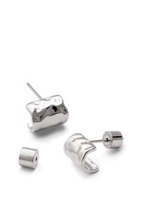 Pendientes de plata con un diseño suave y ondulado. Un pendiente cuenta con un pequeño soporte cilíndrico. La superficie es reflectante y pulida.