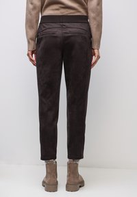 Brązowe, zamszowe spodnie z elastycznym pasem i tylnymi kieszeniami, z prostym krojem nogawki i delikatnym połyskiem.