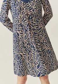 Navyblaues Kleid mit einem beigen Blattmuster, langen Ärmeln und einer gerafften Taille, mit lockerem Schnitt und knielanger Länge.
