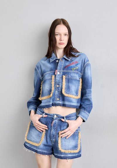 Denim cropped takki, jossa on fringe-reunustetut taskut, brodeerattu teksti ja napit. Yhdistetty yhteensopivien kuluneiden shortsien kanssa. Sininen väri.