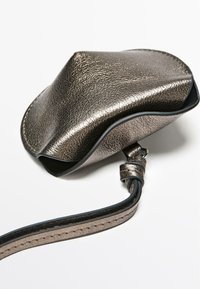 Metaliczna skórzana saszetka z teksturowaną powierzchnią, o zakrzywionym kształcie, czarnym obszyciem i odpinanym paskiem do noszenia.