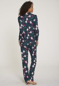 Floral pyjama set met een marineblauwe achtergrond, grote witte en rode bloemen en groene bladeren. Lange mouwen en losse pasvorm van de broek.