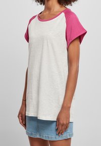 Szary i różowy t-shirt z krótkim rękawem i okrągłym dekoltem, z kontrastowymi rękawami raglanowymi, wykonany z miękkiego materiału, zaprezentowany na modelce.