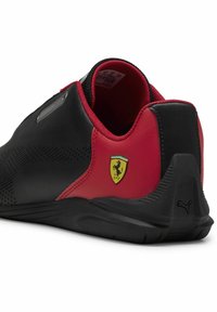 Sort og rød atletisk sko med perforerede detaljer, en tekstureret sort hæl og et Ferrari-logo på siden. Fremstillet af syntetisk materiale.