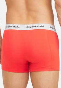 Rote Boxershorts mit einem weißen Bund, auf dem "Originals Studio" in Schwarz gedruckt ist. Glatter, dehnbarer Stoff mit einer enganliegenden Passform.