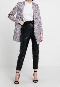 Americana de tejido de tweed en rosa y negro con detalles de flecos, combinada con pantalones de cuero negro de cintura alta y sandalias negras de tacón.