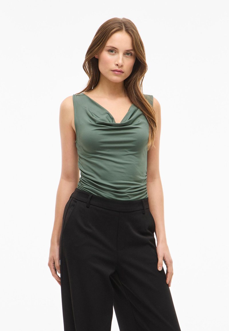 Top verde sin mangas con escote drapeado y textura fruncida, combinado con pantalones negros de tiro alto con bolsillos laterales.