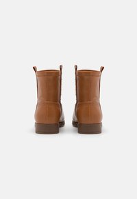 Bottines en cuir marron avec une texture lisse, des languettes à l'arrière et une semelle brune basse. Présentent des coutures décoratives sur les côtés.