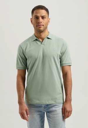 Polo skjorte i myk grønn bomull med korte ermer, v-hals krage og en subtil logo på brystet. Kombinert med lyseblå jeans.