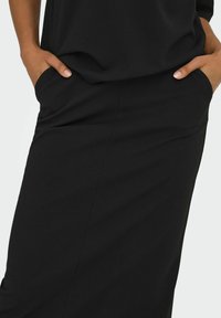 Zwarte kleding met een gladde textuur en zijzakken, met een ontspannen ontwerp dat een strakke silhouet en minimale naden toont.
