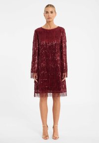 Bordeaux paillettenjurk met franjes, lange mouwen, ronde hals en een knielange zoom, gecombineerd met gouden enkelschoenen.