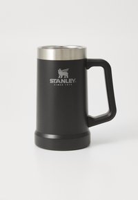 Musta ruostumattomasta teräksestä valmistettu muki, jossa on kaareva runko, hopeinen reuna ja kestävä kahva; lähellä ykköstä on "Stanley"-logo.
