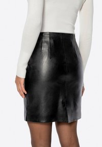 Minigonna in pelle nera con design aderente, caratterizzata da una texture liscia, una lucentezza sottile e due pieghe posteriori per un dettaglio aggiuntivo.