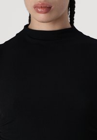 Melnas ribotas turtlenecka blūze ar augstu kakla izgriezumu un pieguļošu piegriezumu. Gluda tekstūra ar minimālu apdari.