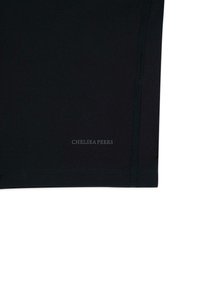 Pantalones cortos deportivos negros con textura suave, costuras cosidas y un logotipo visible de "CHELSEA PEERS" en un color gris contrastante.