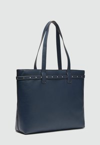 Borsa tote in pelle blu navy con una forma strutturata, dotata di due manici piatti e una fila di borchie dorate lungo il bordo superiore.