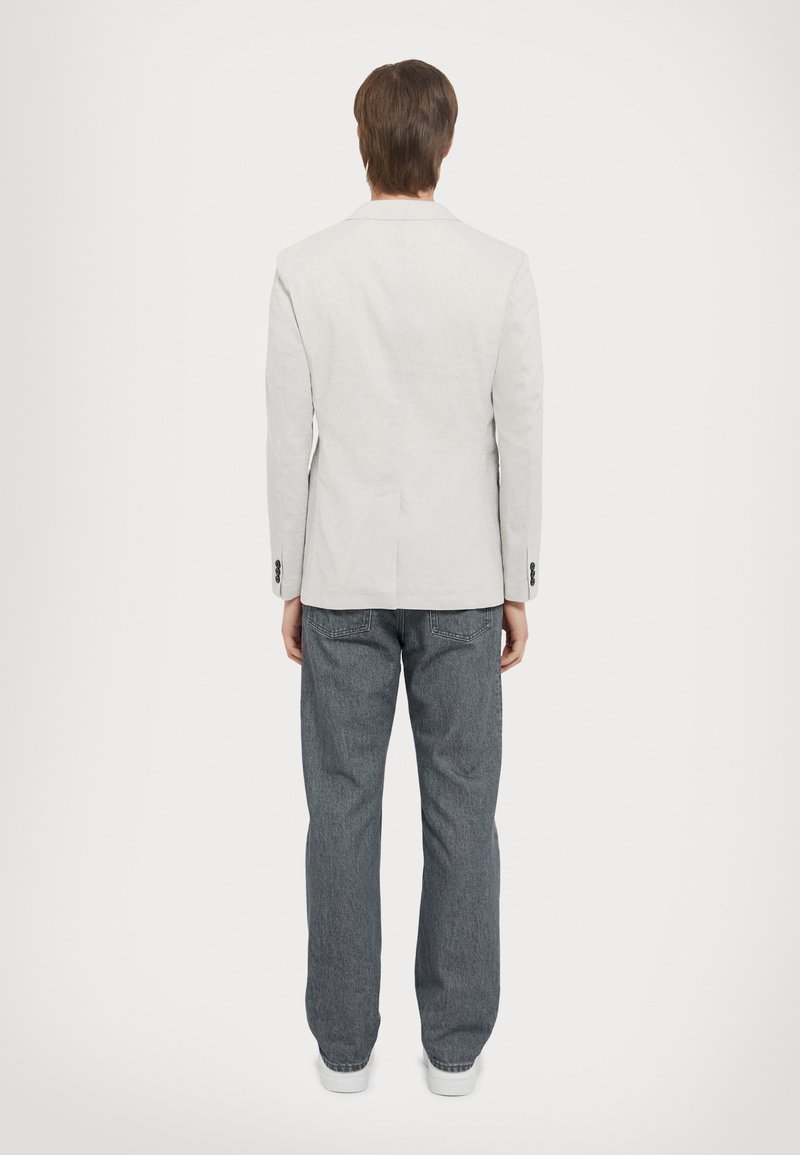 Blazer grigio chiaro con una sola apertura, abbinato a jeans in denim scuro loose. L'outfit presenta un design pulito e minimalista e una sartoria classica.