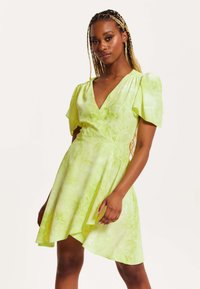 Green tie-dye dress with short puff sleeves, V-neckline, and asymmetrical hem; made of lightweight fabric with a smooth texture.