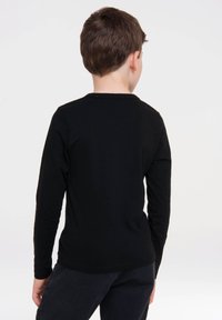 Schwarzes Langarmshirt mit rundem Ausschnitt, glatter Textur und geradem Schnitt, kombiniert mit dunklen Hosen. Ansicht von hinten.