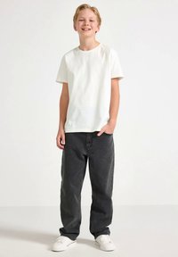 Hvit bomulls-T-skjorte, svarte vide jeans og hvite joggesko. Antrekket har et enkelt design med en avslappet silhuett og nøytrale farger.