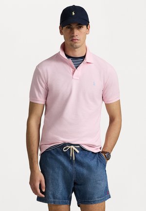 Light pink polo shirt with short sleeves and a buttoned collar, worn over a navy and white striped shirt, paired with denim shorts.