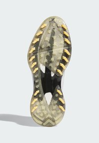 Kengän pohja, jossa on musta-keltainen kuvioitu muotoilu. Siinä on nastoja pidon parantamiseksi, jotka on yhdistetty naamiointikuviin ja keskellä on uritus.