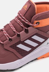 Bordowe buty do wędrówek z siateczkową cholewką, gumową podeszwą, białymi akcentami w postaci trzech pasków i pomarańczowymi detalami. Posiadają wzmocnione przelotki i system sznurowania.