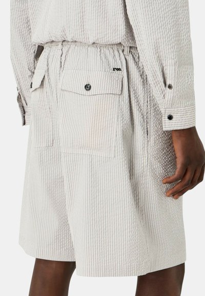 Pantaloni corti grigio chiaro con sottili righe verticali. Presentano una cintura elasticizzata, due tasche laterali e un tessuto testurizzato.