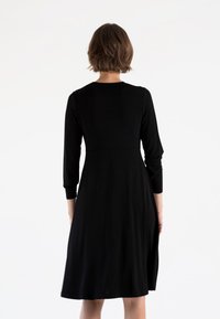 Abito nero con maniche lunghe, corpetto aderente e gonna svasata. Realizzato in un tessuto liscio, presenta un colletto rotondo modesto e lunghezza a metà polpaccio.