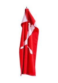 Asciugamano rosso realizzato in tessuto spesso, con una grande silhouette bianca di una figura in salto. L'asciugamano pende da un piccolo gancio metallico.