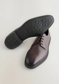 Chaussures en cuir marron foncé avec une finition texturée, bout pointu et semelle en caoutchouc noir présentant des motifs circulaires et des rainures.