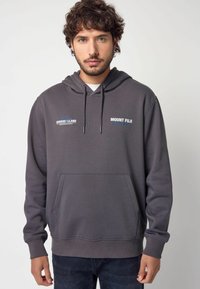 Sweat à capuche gris avec une poche frontale, un cordon de serrage et des accents de texte portant les inscriptions « MONT FUJI » et « ÎLE HONSHU ». Texture de tissu lisse.