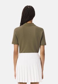 Polo de color verde oliva con cuello, de manga corta, combinado con una falda blanca con pliegues. Enfoque en un diseño simple y limpio.