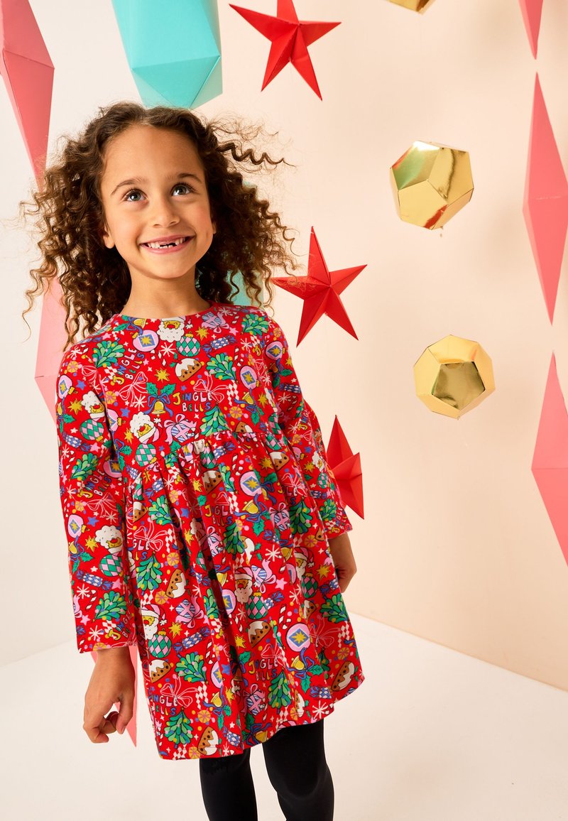 Red long-sleeve dress with festive patterns featuring Christmas elements, complemented by elastic waist and pleated design. Black leggings worn.