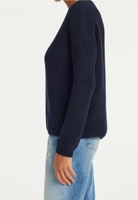Granatowy sweter z dzianiny o prążkowanej fakturze, z długimi rękawami i okrągłym dekoltem, zestawiony z jasnoniebieskimi dżinsami.