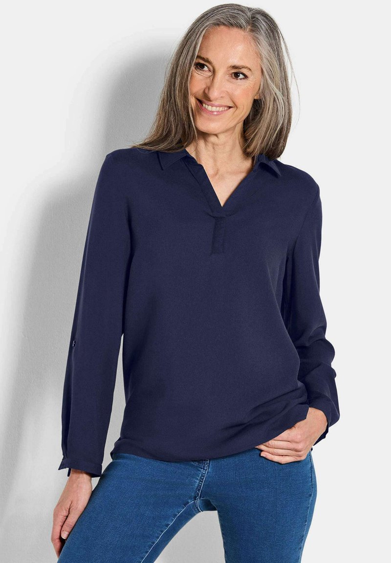 Camicia a maniche lunghe blu navy con scollo a V, tessuto morbido, polsini con bottone e vestibilità comoda, abbinata a jeans blu.