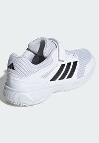 Biele športové topánky s vrchnou časťou z materiálu sieťoviny, nastaviteľným pásikom a tromi čiernymi pruhmi po stranách. Zakrivený tvar a textúrovaná podrážka.