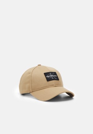 Beige baseball cap with curved brim and black patch featuring "Calvin Klein Jeans" logo on the front panel.