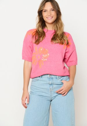 Short-sleeve pink knit sweater with floral design in orange and sequins, paired with light blue high-waisted jeans.