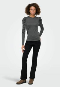 Grå langærmet top med puffede ærmer, parret med sorte tætsiddende bukser og brune ankelstøvler. Glat stof med et tætsiddende design.